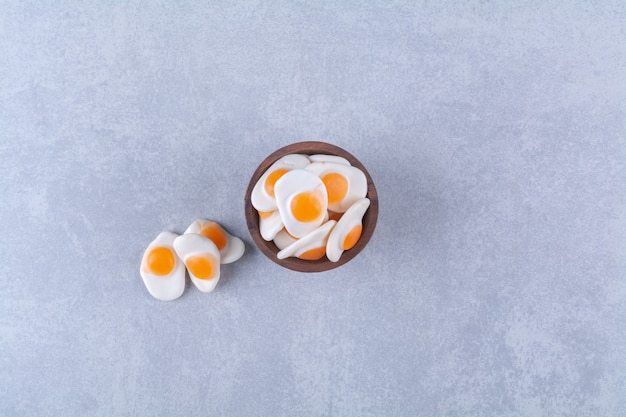 Un cuenco de madera lleno de huevos dulces fritos en gelatina sobre fondo gris. Foto de alta calidad