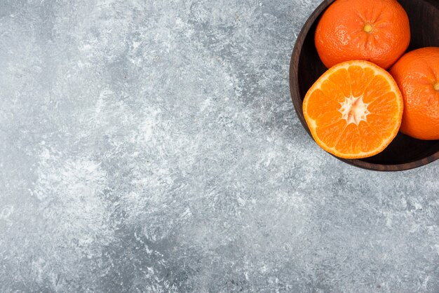 Un cuenco de madera lleno de jugosas frutas naranjas en la mesa de piedra.