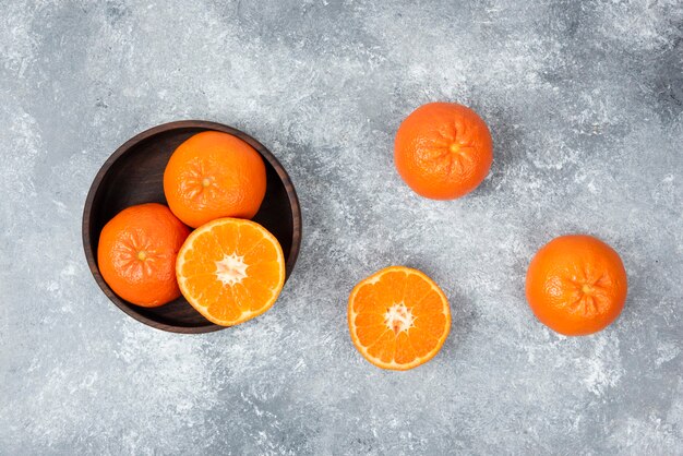 Un cuenco de madera lleno de jugosas frutas naranjas en la mesa de piedra.