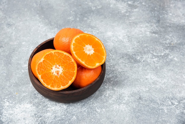 Un cuenco de madera lleno de jugosas frutas naranjas en la mesa de piedra.