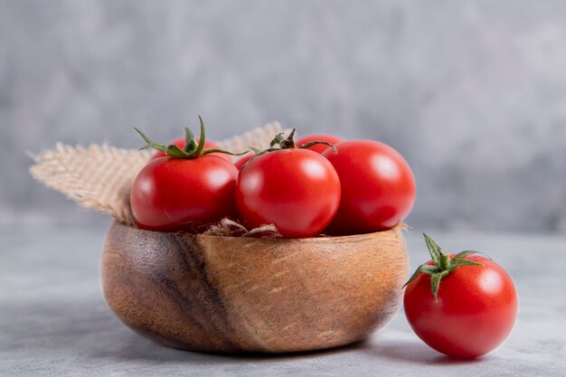 Un cuenco de madera lleno de jugosos tomates rojos frescos colocados sobre la mesa de piedra. Foto de alta calidad