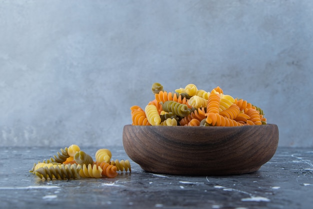 Foto gratuita un cuenco de madera lleno de macarrones multicolores sobre un fondo gris.