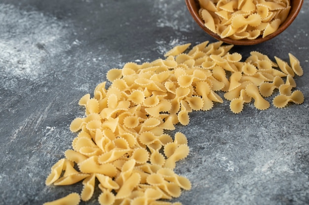 Un cuenco de madera lleno de macarrones tostados de farfalle crudo.