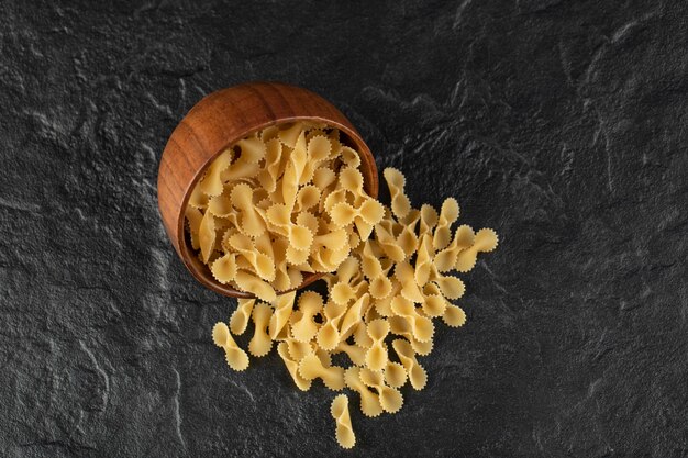 Un cuenco de madera lleno de macarrones tostados de farfalle crudo.