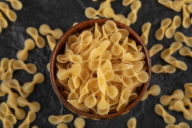 Un cuenco de madera lleno de macarrones tostados de farfalle crudo.