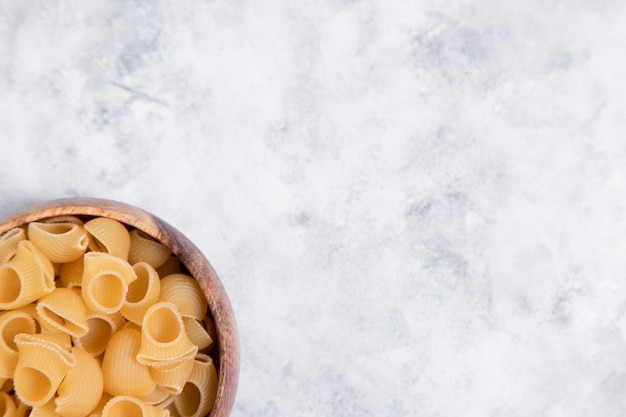 Cuenco de madera lleno de pasta cruda Conchiglie colocado sobre fondo de mármol. Foto de alta calidad