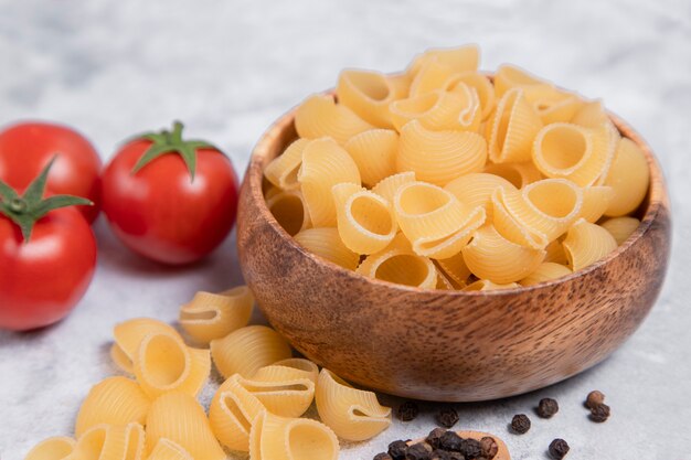 Cuenco de madera lleno de pasta cruda Conchiglie colocado sobre fondo de mármol. Foto de alta calidad