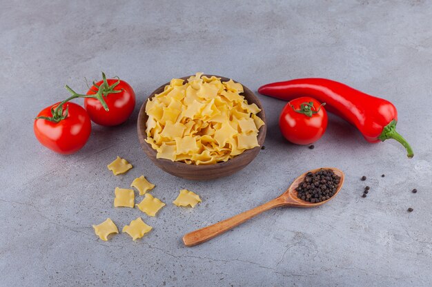 Un cuenco de madera lleno de pasta de ravioles sin cocer con tomates rojos frescos y ají.