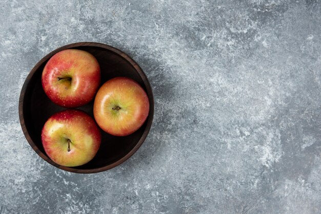 Cuenco de madera de manzanas frescas brillantes sobre superficie de mármol.