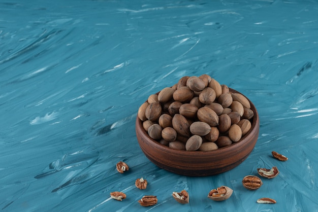 Cuenco de madera de nueces orgánicas sin cáscara sobre superficie azul.