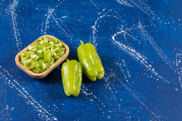 Cuenco de madera de pimientos verdes en rodajas y pimientos enteros.