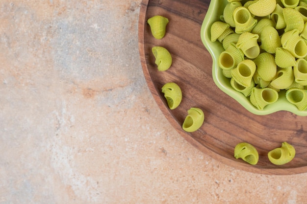 Foto gratuita un cuenco de madera con plato verde de macarrones verdes sin preparar.