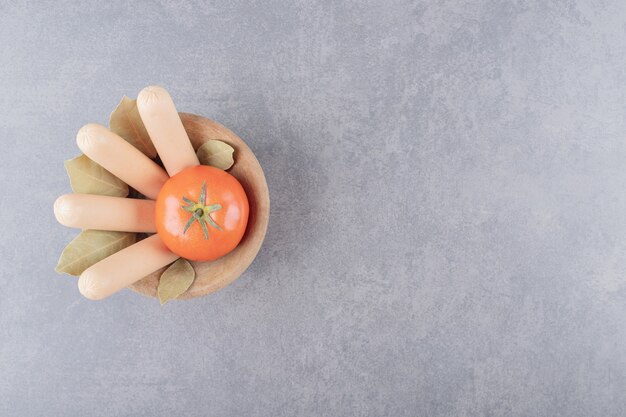 Un cuenco de madera de salchichas hervidas con tomate rojo y hojas de laurel.