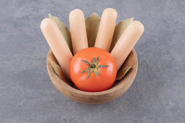 Un cuenco de madera de salchichas hervidas con tomate rojo y hojas de laurel