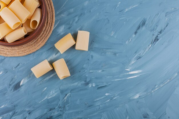 Un cuenco de madera de tubo de pasta seca cruda sobre una mesa azul.