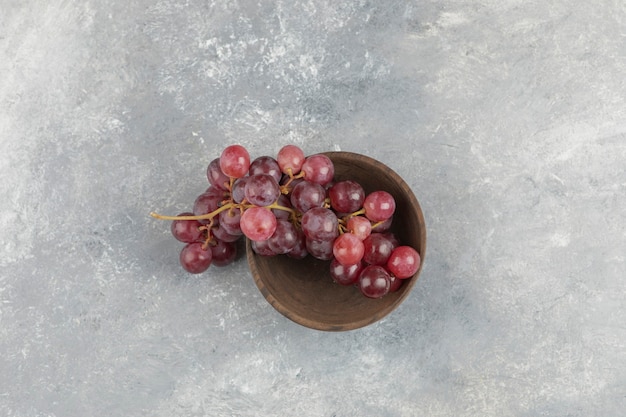 Foto gratuita cuenco de madera de uvas rojas frescas sobre superficie de mármol.