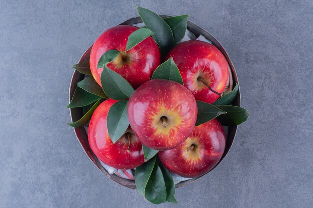 Un cuenco de manzanas con hojas sobre la mesa de mármol.