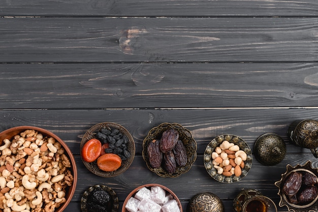 Foto gratuita cuenco metálico con dulce lukum; frutos secos y nueces en el escritorio de madera negro para ramadan