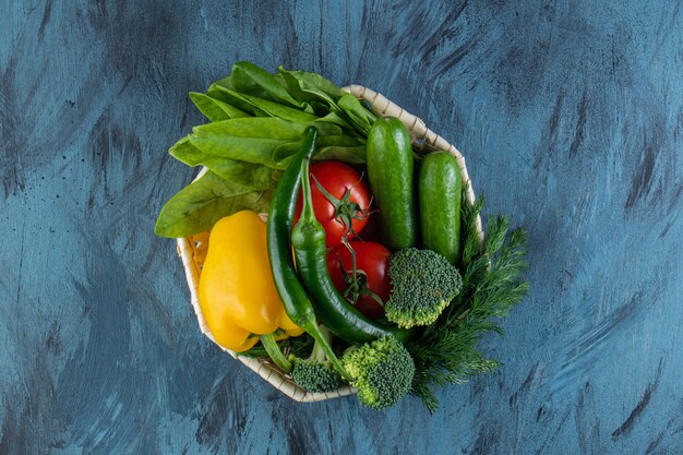 Cuenco de mimbre de verduras orgánicas frescas sobre superficie azul. .