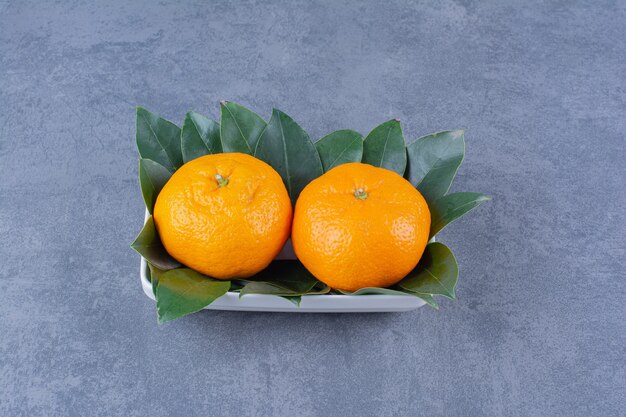 Un cuenco de naranjas y hojas sobre la mesa de mármol.