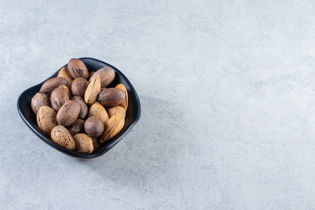 Cuenco negro lleno de almendras sin cáscara y nueces sobre piedra.