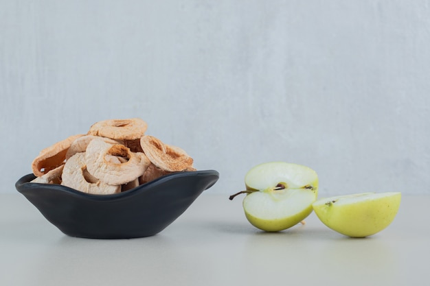 Un cuenco negro lleno de manzanas secas con rodajas de manzana fresca.