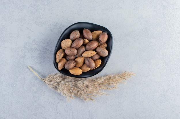 Cuenco negro lleno de nueces y almendras sin cáscara sobre fondo de piedra.