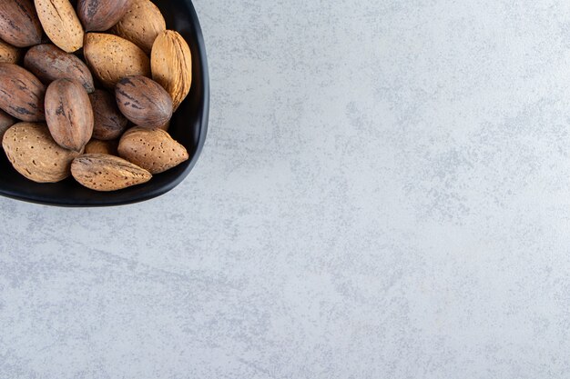 Cuenco negro lleno de nueces y almendras sin cáscara sobre fondo de piedra.