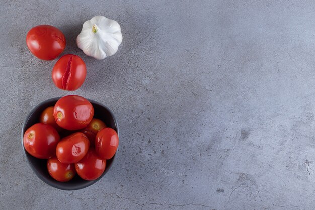 Cuenco oscuro de tomates encurtidos colocados sobre la mesa de piedra.