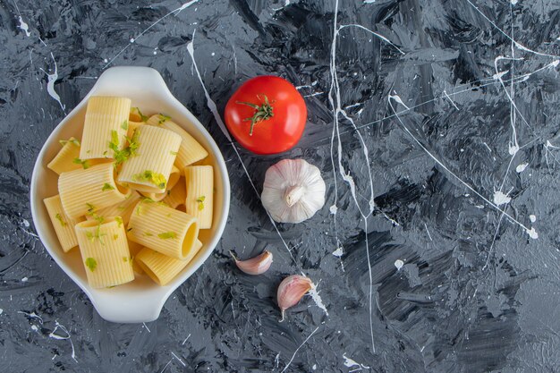 Cuenco de pasta calamarata hervida con verduras sobre fondo de mármol.