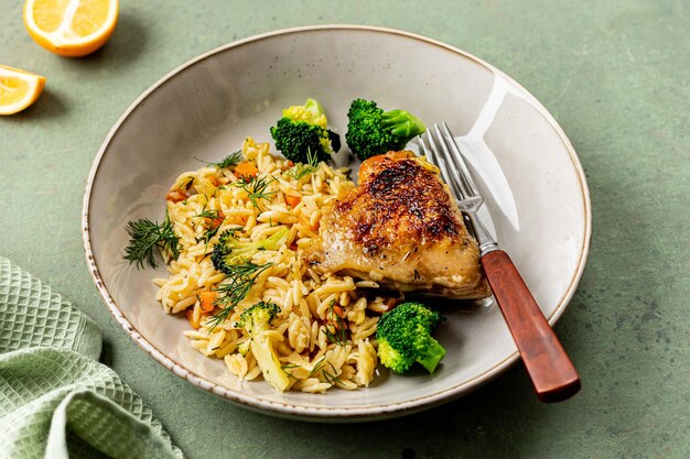 Cuenco con pasta de pollo o orzo con verduras sobre un fondo verde