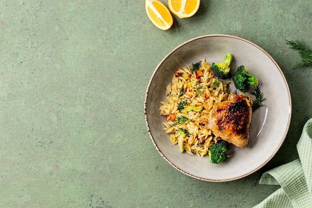 Cuenco con pasta de pollo orzo con verduras al estilo mediterráneo sobre un fondo verde