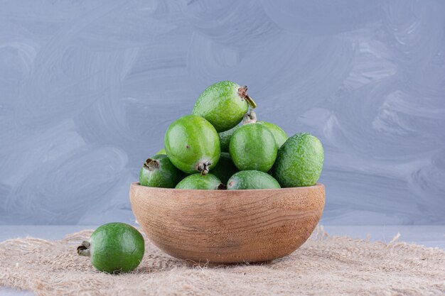 Cuenco pequeño de feijoas sobre un trozo de tela sobre fondo de mármol.