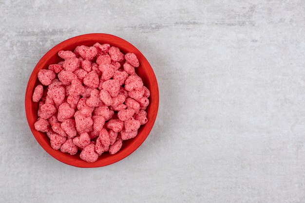 Cuenco rojo lleno de cereales rosas en la mesa de piedra.