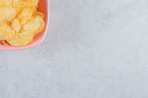 Cuenco rosa de deliciosas patatas fritas crujientes sobre fondo de piedra.