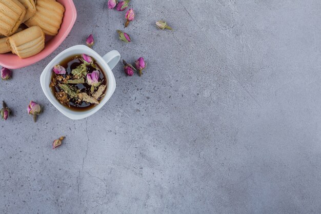 Cuenco rosa de galletas dulces y taza de té caliente sobre fondo de piedra.