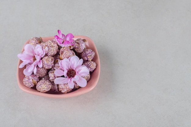 Cuenco rosa lleno de palomitas de maíz con sabor decorado con flores sobre mesa de mármol.