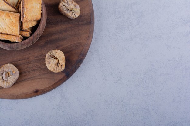 Cuenco de sabrosas galletas crujientes e higos secos sobre tabla de madera.