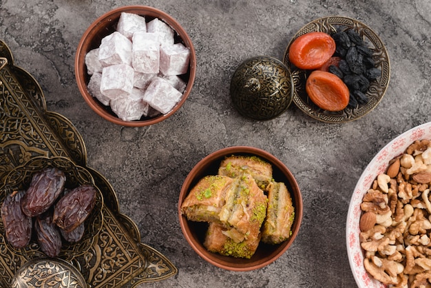 Cuenco de tierra de lukum; baklava; fechas; Frutos secos y frutos secos sobre hormigón gris.