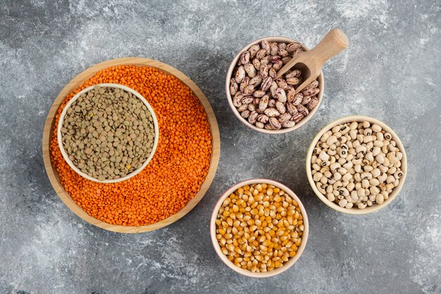 Cuencos coloridos de varios frijoles crudos, lentejas y callos sobre la superficie de la mesa de mármol.