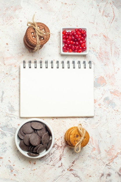 Foto gratuita cuencos de cuaderno de vista superior con bayas y galletas de chocolate atadas con una cuerda en la mesa gris claro