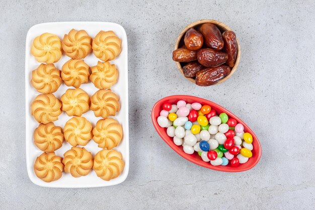 Cuencos de dátiles y caramelos junto a un paquete de galletas crujientes en un plato sobre fondo de mármol. Foto de alta calidad