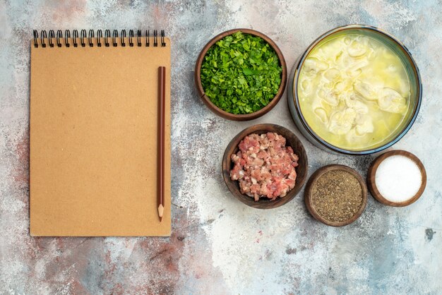 Cuencos de dushbara de vista superior con diferentes especias verduras lápiz de carne en el cuaderno en la superficie desnuda