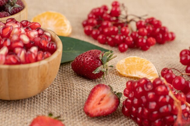 Cuencos de granada y frambuesa con un surtido de frutas esparcidas sobre fondo textil. Foto de alta calidad