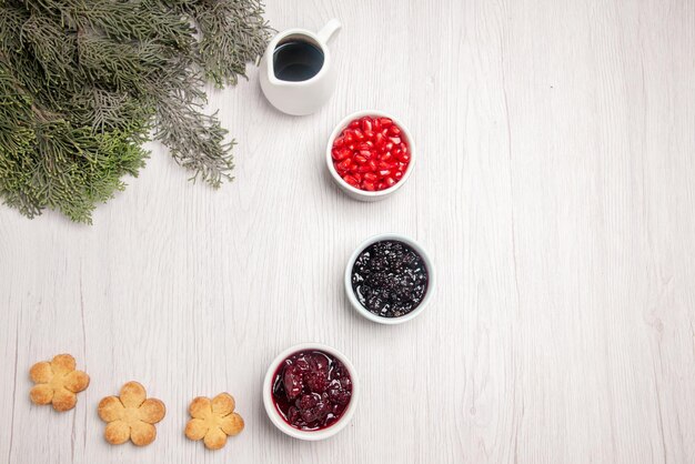 Cuencos de granada de vista superior de galletas de mermelada de granada junto a las ramas del árbol de Navidad en la mesa