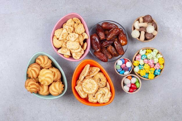 Cuencos llenos de caramelos, galletas, galletas saladas, dátiles y setas de chocolate sobre fondo de mármol. Foto de alta calidad