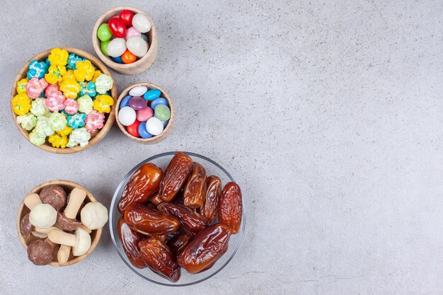 Cuencos llenos de dátiles, setas de chocolate y caramelos de colores sobre la superficie de mármol