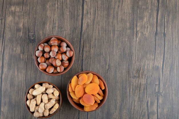 Cuencos de madera llenos de nueces saludables con frutos secos de albaricoque sobre mesa de madera.