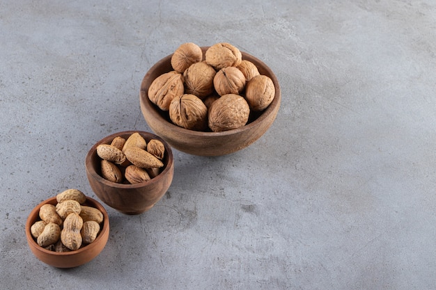 Cuencos de madera de nueces, almendras y cacahuetes sin cáscara orgánicos sobre fondo de piedra.