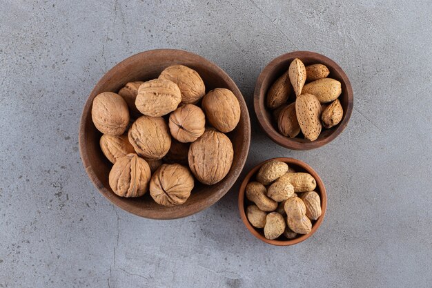 Cuencos de madera de nueces, almendras y cacahuetes sin cáscara orgánicos en la superficie de la piedra